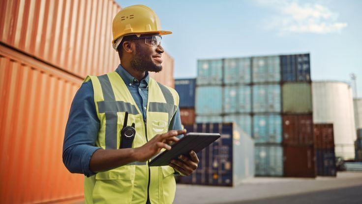 Warehouse logistics worker with tablet beside stacked containers